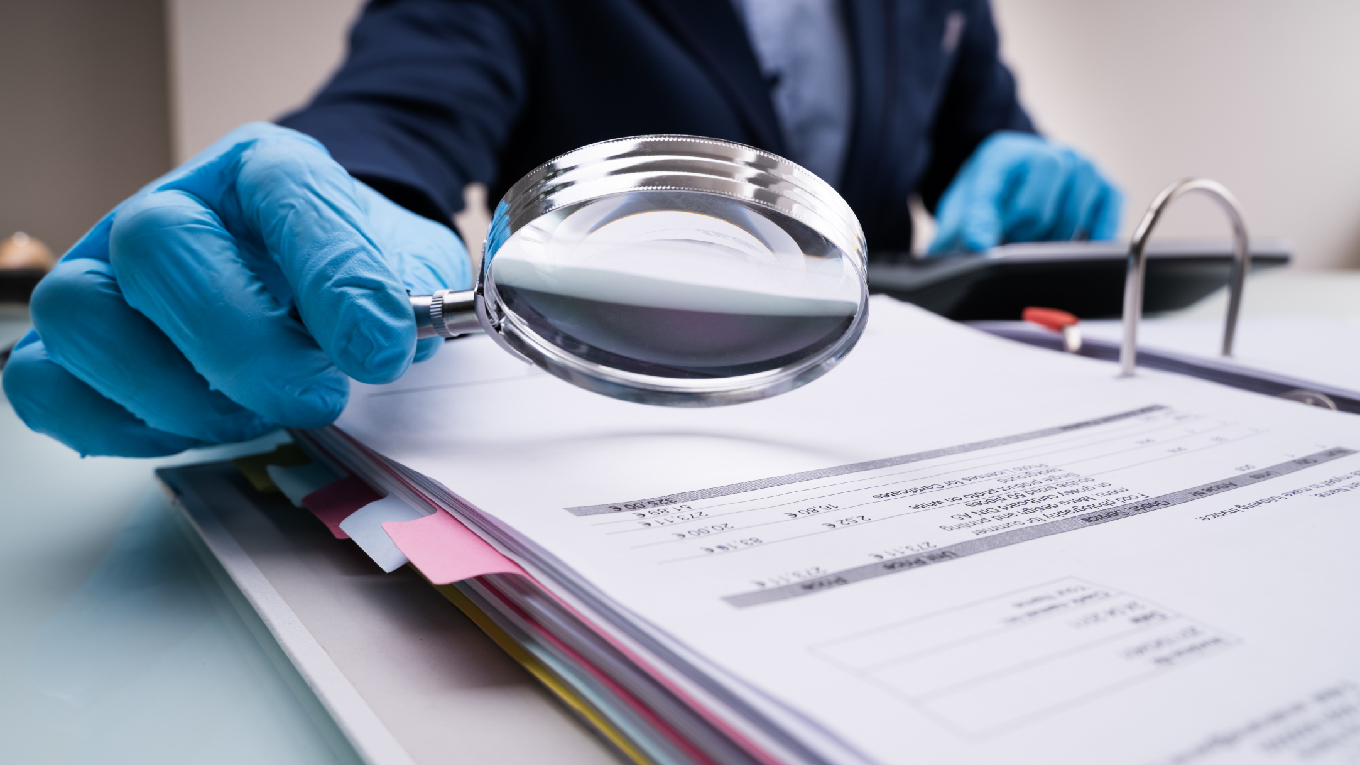 Profissional examinando documentos financeiros com lupa e luvas, representando a análise técnica da perícia contábil