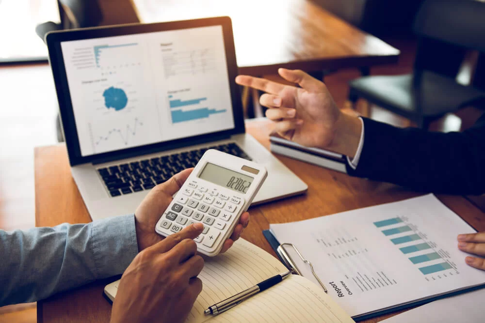 Profissionais analisando relatórios financeiros em laptop, calculadora e documentos sobre a mesa, representando contabilidade e consultoria empresarial
