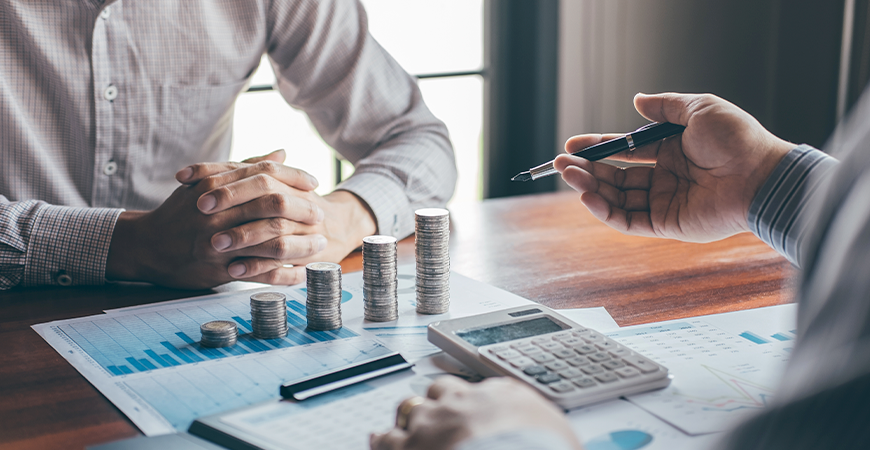 Reunião de negócios com pilhas de moedas, calculadora e gráficos sobre a mesa, representando planejamento e recuperação tributária